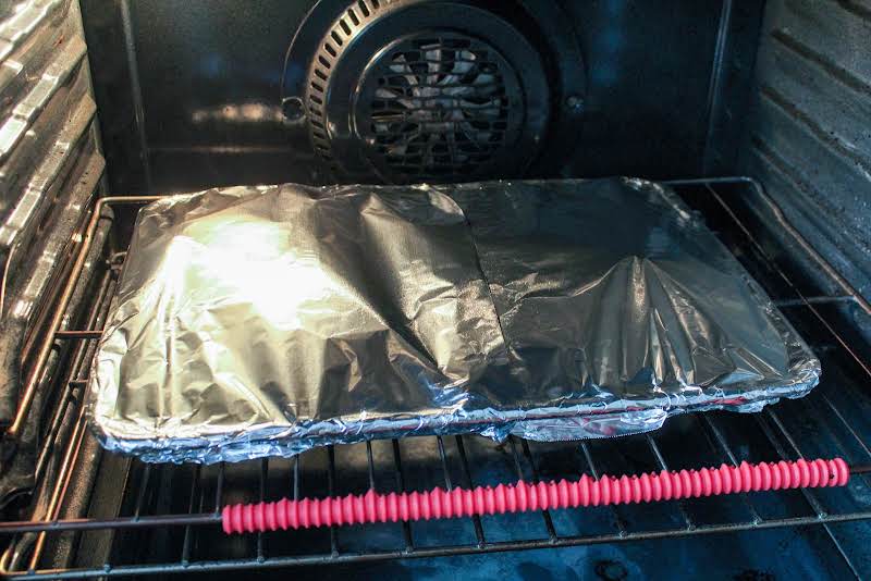 Baking Sheet With Vegetables Covered With Foil In The Oven.