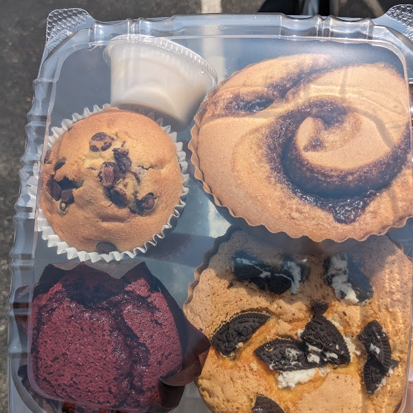 Chocolate chip muffin, red velvet muffin, cinnamon roll with frosting on the side, cookies n cream pastry