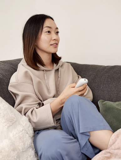 A woman sits on the sofa, holding the Chromecast with Google TV remote