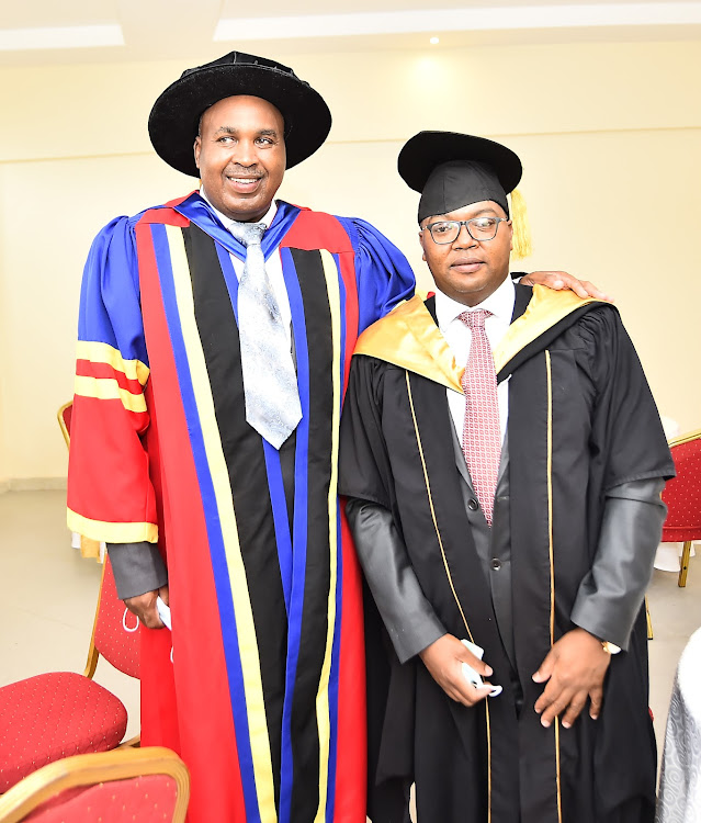 Mount Kenya University founder and chairman Simon Gicharu congratulates Lands PS Nicholas Muraguri after he graduated at the university.