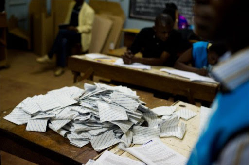 Election officials sit behind a pile of presidential ballot papers emptied onto a table at a polling station in Lubumbashi on November 28, 2011.