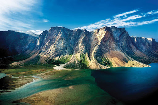 View of a steep-sided mountain touched by blue waters at Torngat Mountains National Park at the northern tip of Newfoundland and Labrador.