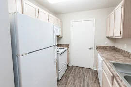 Galley kitchen with light wood cabinets, brown countertops, white appliances, wood inspired flooring, and laundry closet