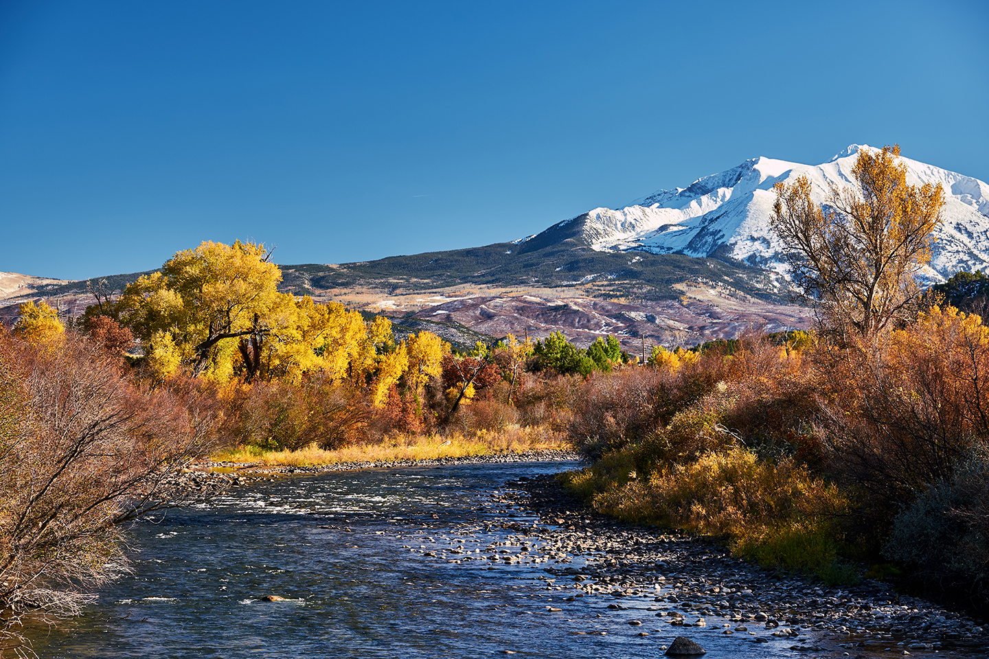 A view of the snow-capped Rocky Mountains with a stream leading up to them outside Basalt