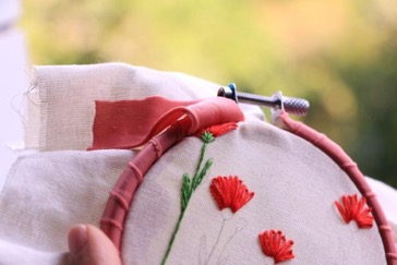 Red embroidery hoop holding white fabric with red flowers stitched on with green stems.