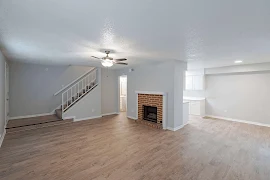 Open living area with wood inspired floors, brick fireplace, stairway to upper level, and neutral color scheme throughout