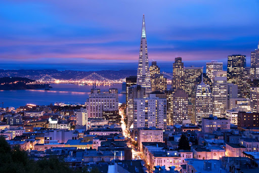 San-Francisco-skyline-at-dusk - A view of San Francisco's illuminated skyline and the Bay Bridge at dusk.