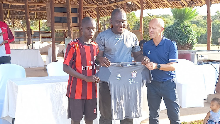 A young player receives a Bayern Munich jersey from Base Titanium's government and community relations superintendent and former head coach of FC Bayern Seniors and Youth Academy Michael Hilbig in Kwale county on Saturday, September 9, 2023.