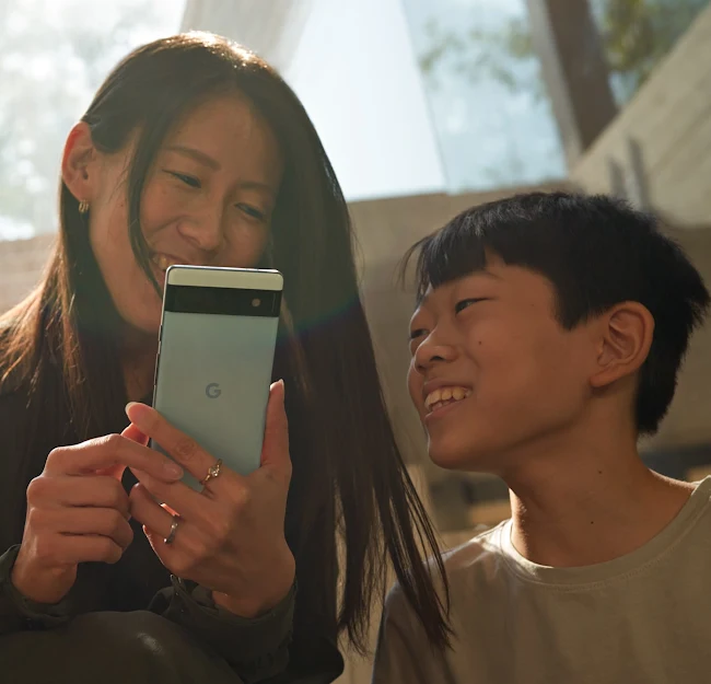 A parent and child enjoy content on a Sage green Pixel 6a phone outside