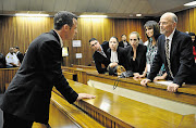 ACROSS THE DIVIDE: Oscar Pistorius talks to family members during a break in his murder trial. Those in the picture include his brother Carl, far left, his sister Aimee, next to Carl, and his uncle Arnold, on the right.