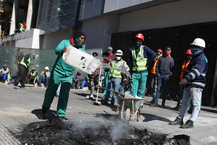 Workers at a construction site clear a barricade as private security monitors the scene at Benmore in Sandton, Johannesburg. A group of construction workers protested on Wednesday morning over a wage dispute and attacked a security guard.