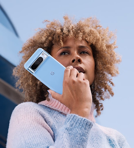 A person gazes around on a hiking trail. In their left hand is a Pixel 8 Pro in a Pixel 8 Pro Case. They also wear a Pixel smartwatch.