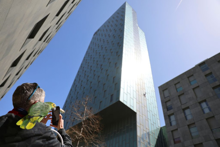 A man with a parrot observes as George King, the man who climbed the Shard, climbs the Hotel Melia Barcelona Sky in Barcelona, Spain, on April 2 2021.