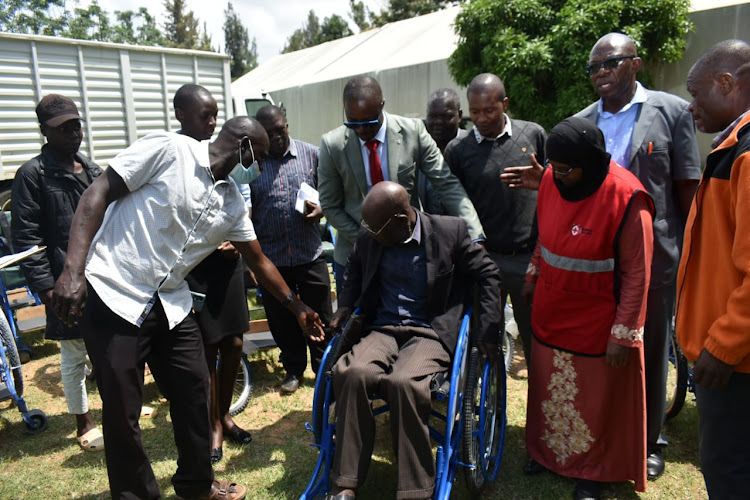 Bungoma CEC for Health and Sanitation Dr. Andrew Wamalwa pushing a beneficiary's Wheelchair.