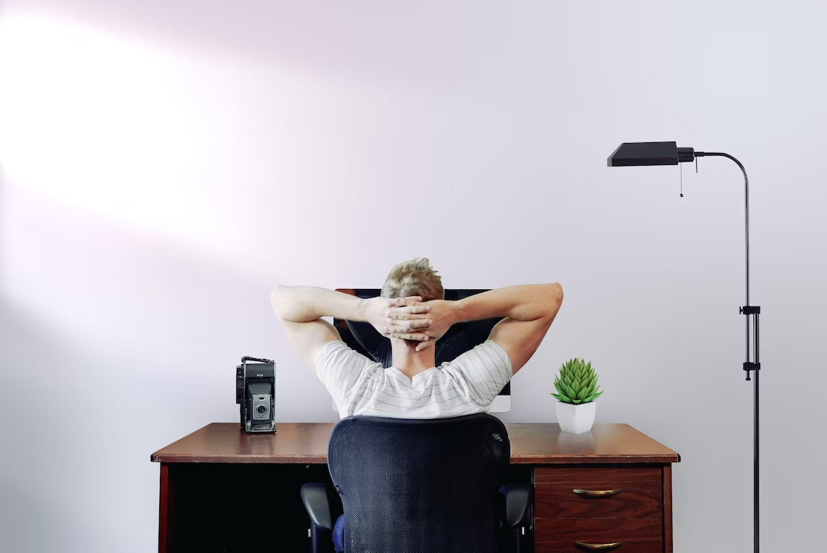 A man holding his head with two hands while sitting on chair looking at computer desk