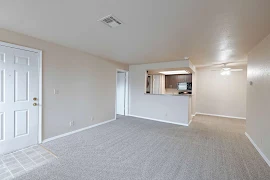 Apartment entry door open to the living and dining area with carpeted flooring, white trim, and tan walls throughout 