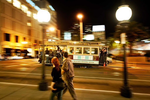 A cable car passes through Union Square in San Francisco at dusk.