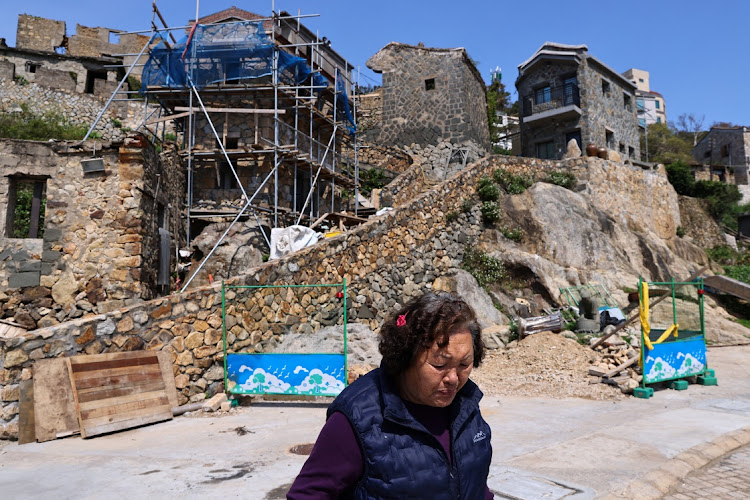 An elder woman walks past a restoration project to protect traditional buildings in Nangan, Taiwan, March 18, 2022. Photo taken March 18, 2022.