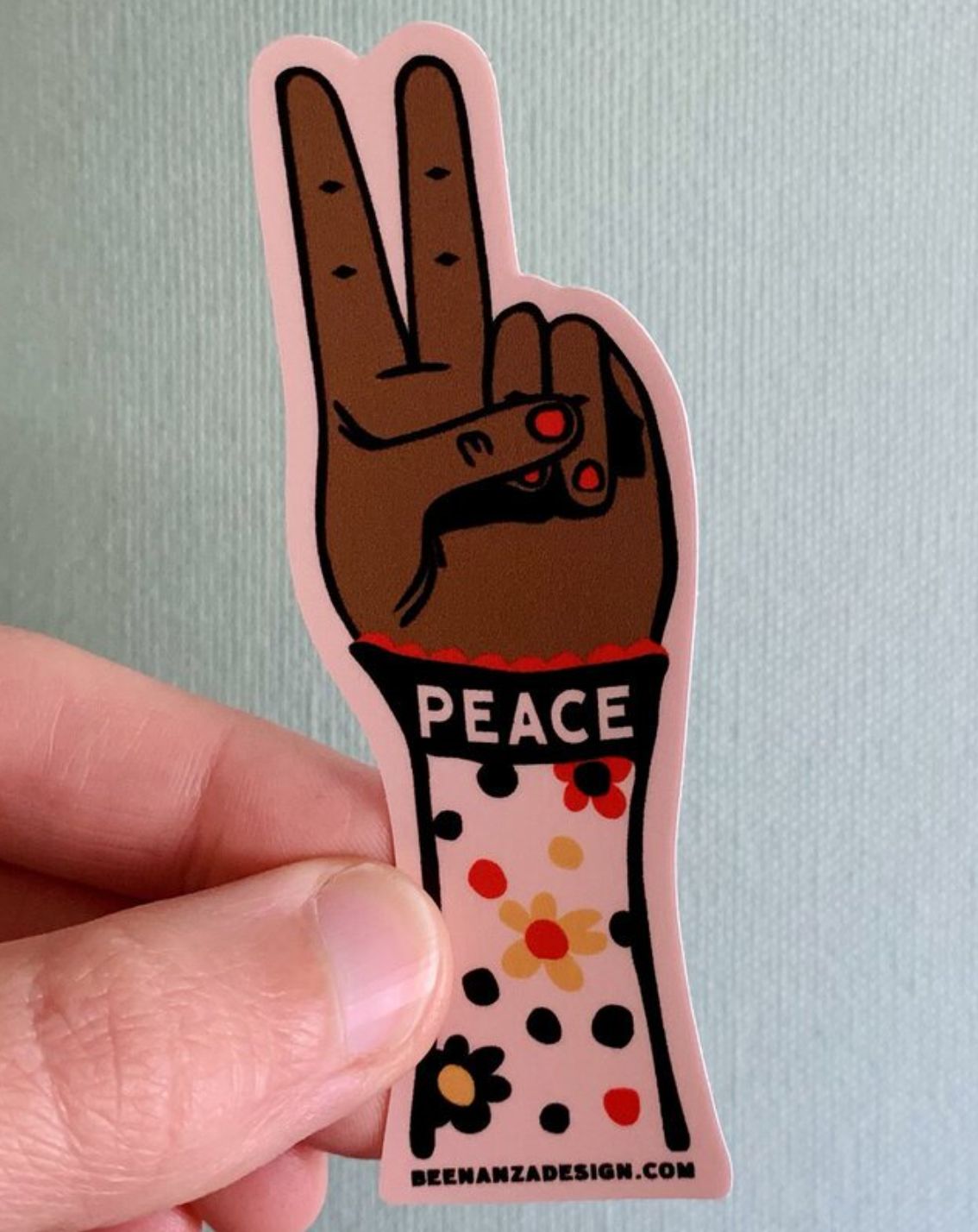 person holding a sticker of a hand giving a peace sign that says "peace" 