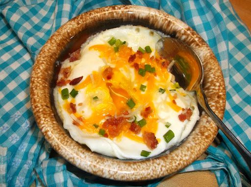 Asiago grits topped with egg, bacon, cheese & chives, in bowl with spoon.