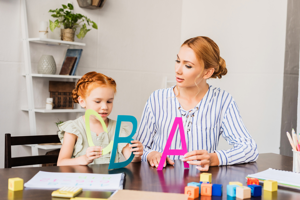 Adult and child practicing letter recognition with large cut-outs of capital letters