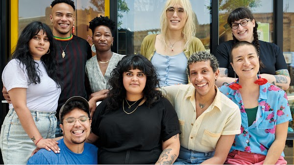Một nhóm chín người thuộc các chủng tộc và giới tính khác nhau đang mỉm cười bên ngoài cửa hàng