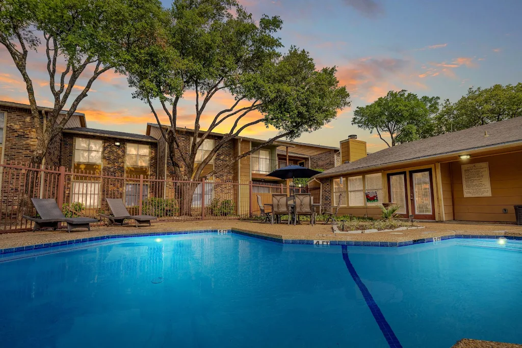 Bella Vista's swimming pool with picnic table and lounge chairs at dusk by apartment buildings