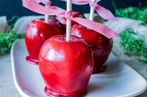 Three cinnamon candy apples on a white plate.