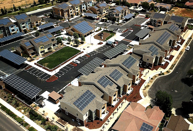 Aerial photo of a housing community with rooftop solar panels and parking lot solar canopies.