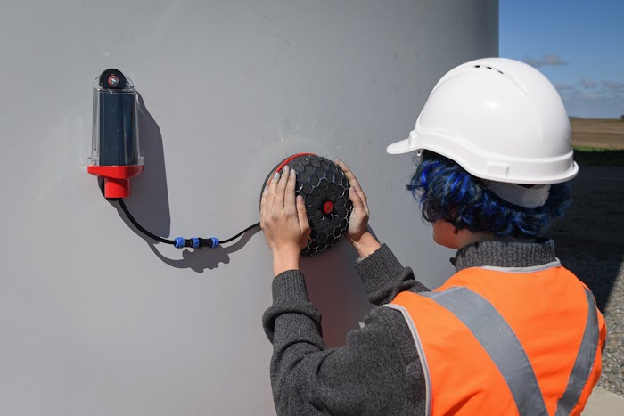 Employee in orange safety vests adjusts equipment on side of a turbine