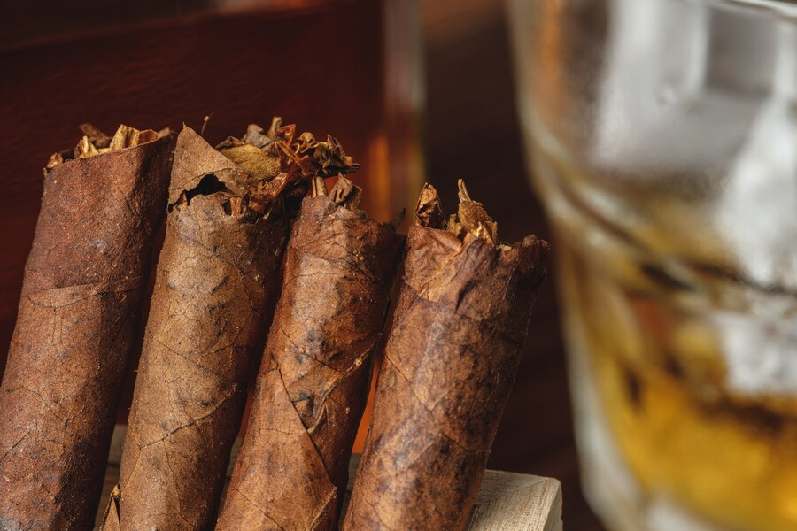 a stack of tobacco on a wooden table with a glass of whiskey