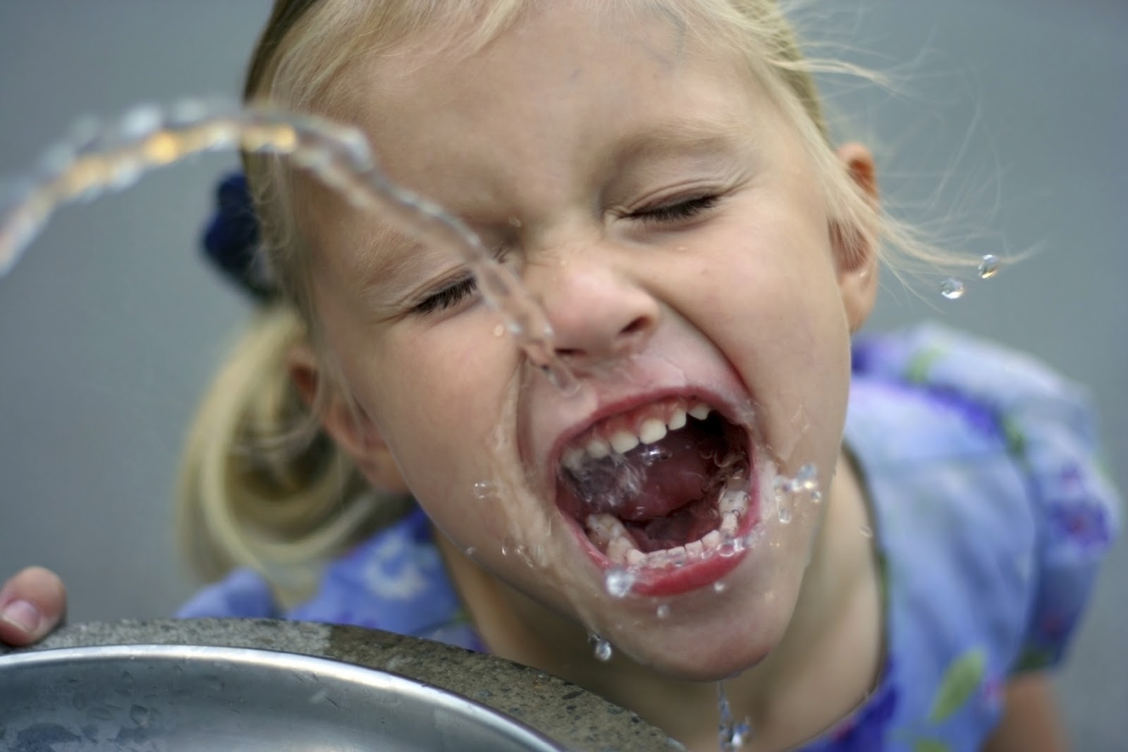 A girl drinking from a water fountain. 
