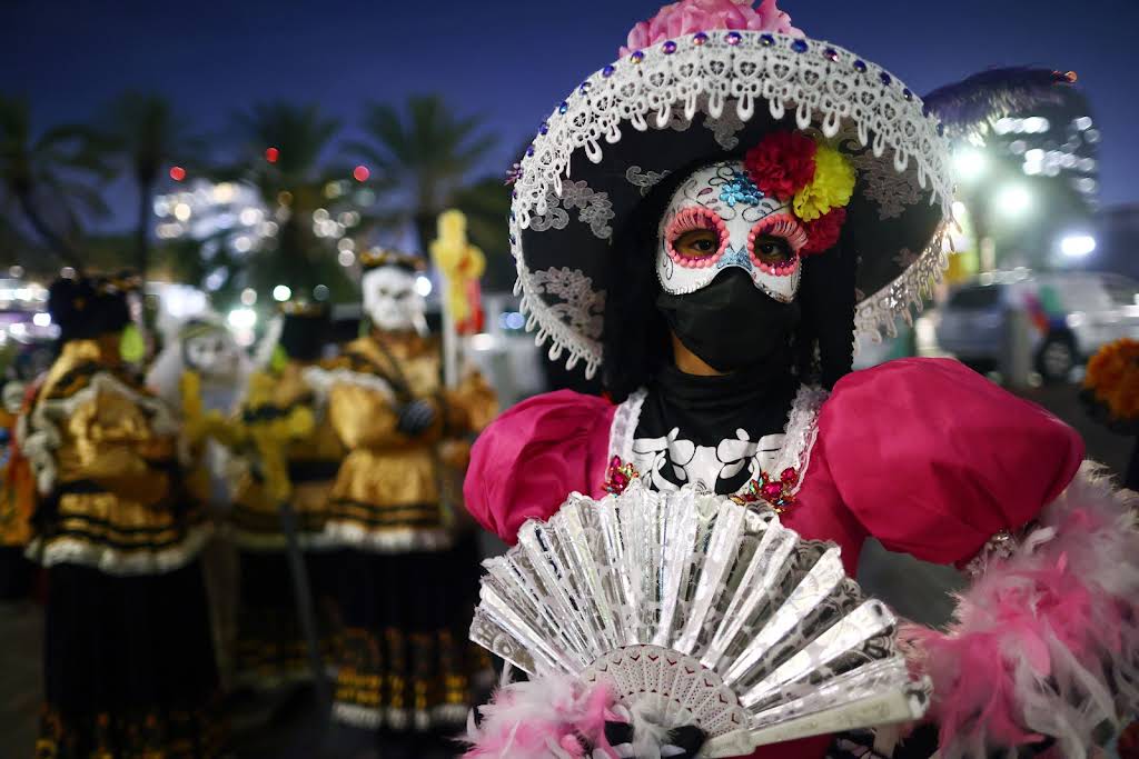 Gümüş yelpaze tutan, La Catrina maskeli, geleneksel elbiseli kişinin fotoğrafı