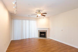 Living room with wood flooring, light walls, white trim, a ceiling fan, corner fireplace with tile surround, and patio door