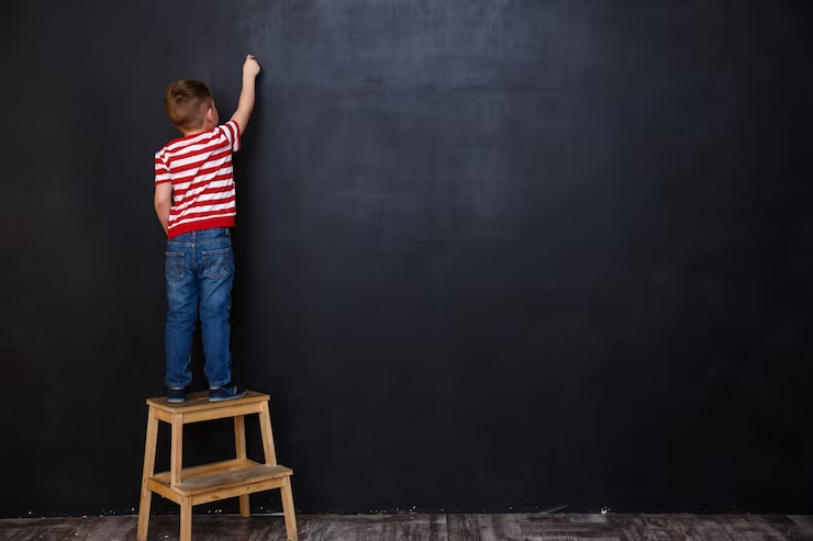 A young boy writing with chalk on a chalkboard.