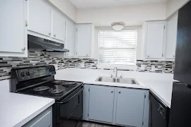 Kitchen with gray bottom cabinets, white upper cabinets, white countertops, and black appliances with a window over the sink 