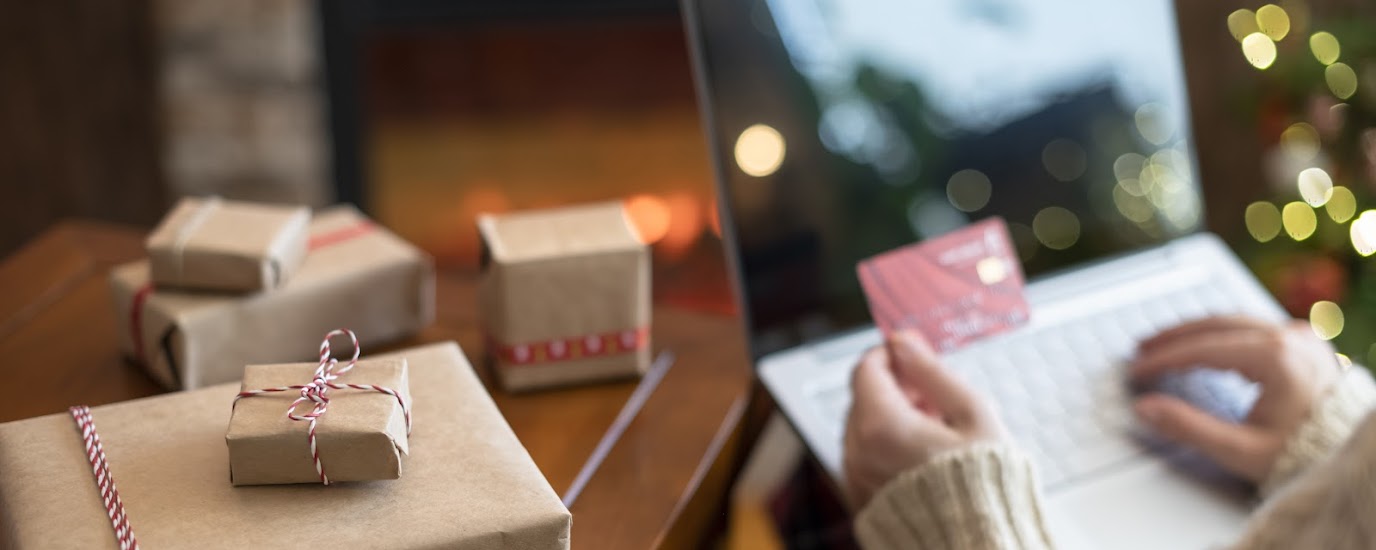 Woman using credit card to do online shopping on a laptop next to holiday gifts.