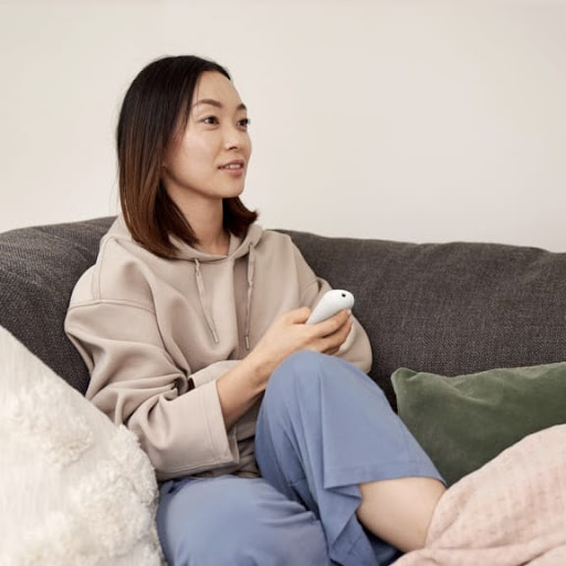 A woman sits on the sofa, holding the Chromecast with Google TV remote