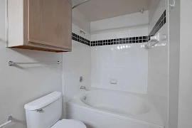 Bathroom with tub/shower combo with tile-inspired walls next to the toilet with a cabinet and towel rod above.