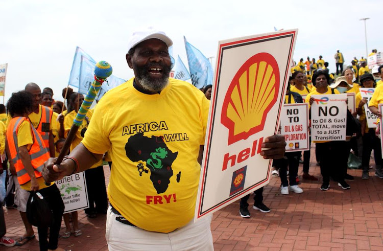 An old man picketing carrying a placard and a knobkerrie saying Shell must not interfere with their oceans.