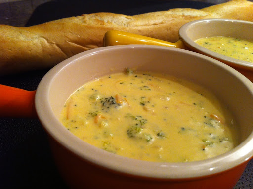 Two bowls of broccoli soup with a French baguette in the background.