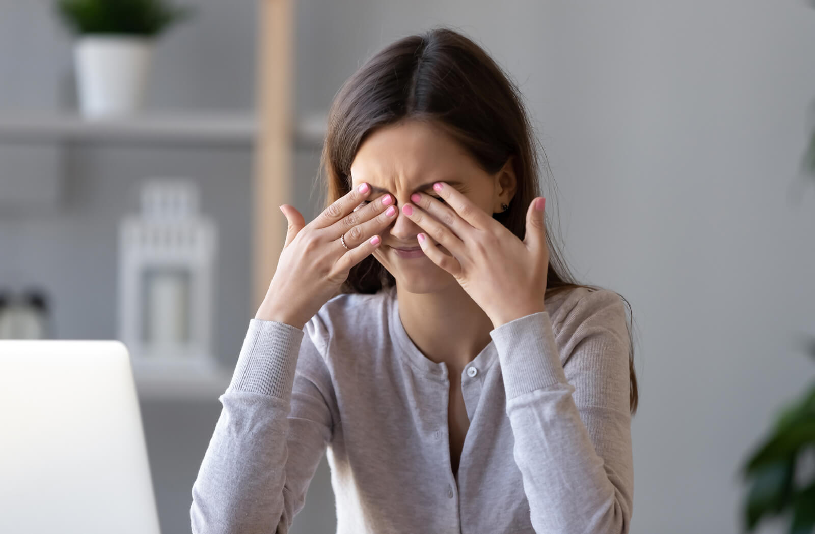 a woman rubs her eyes while working at a computer because she has dry eye