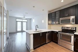 Kitchen with dark brown cabinets, white countertops, stainless steel appliances, wood floors, looking into living room