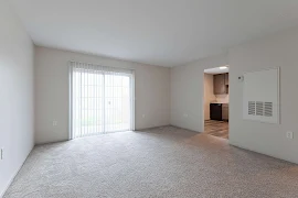 Empty apartment interior with carpeted floor, white walls, and sliding door leading to a balcony.