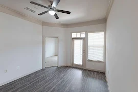 Apartment living room with wood-inspired flooring, a patio door and window with blinds, and a ceiling fan overhead 