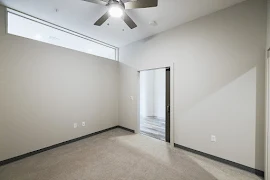 Bedroom with light walls, dark trim, beige carpet, ceiling fan, and sliding door out to hallway