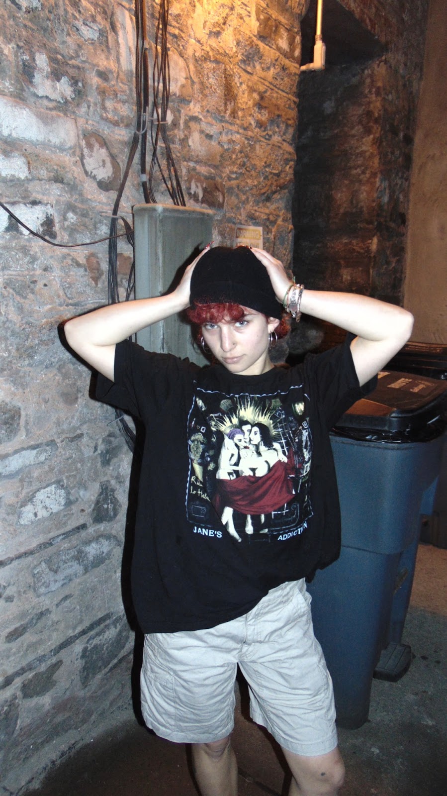 Sydney Levy posing outside wearing a black beanie, band tee, and knee length shorts.