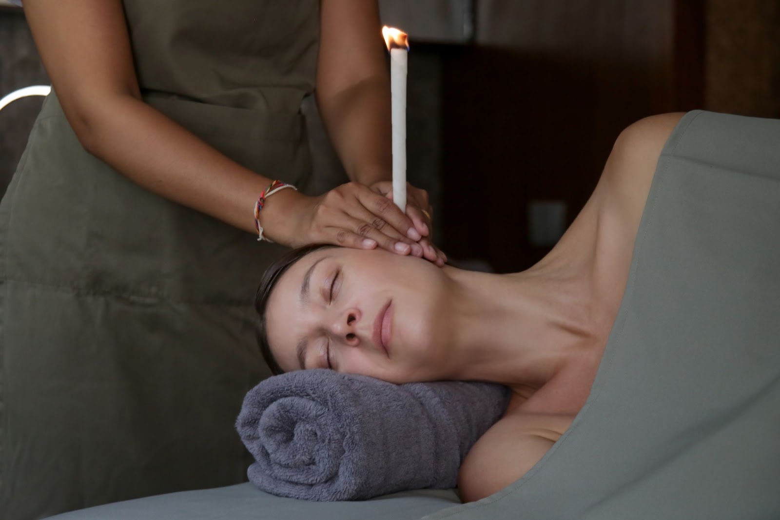 A woman receiving hopi ear candle treatment lying down with her head resting on a pillow.