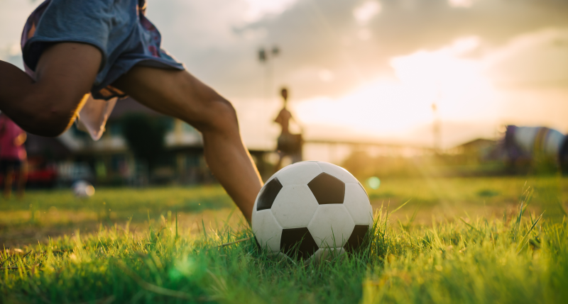 Niño jugando fútbol en cancha con sol