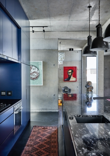 Built-in cupboards painted in a bold Yves Klein royal blue offset the concrete walls and eclectic decor elements.